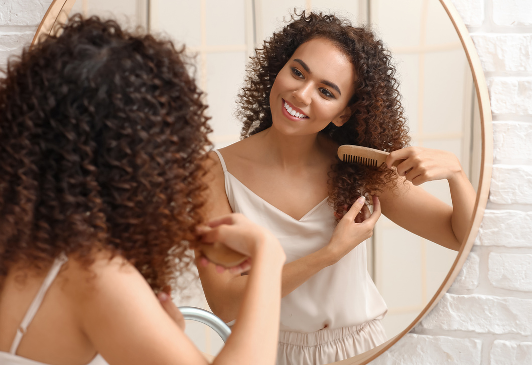 Young African-American Woman Combing Her Hair near Mirror in Bathroom