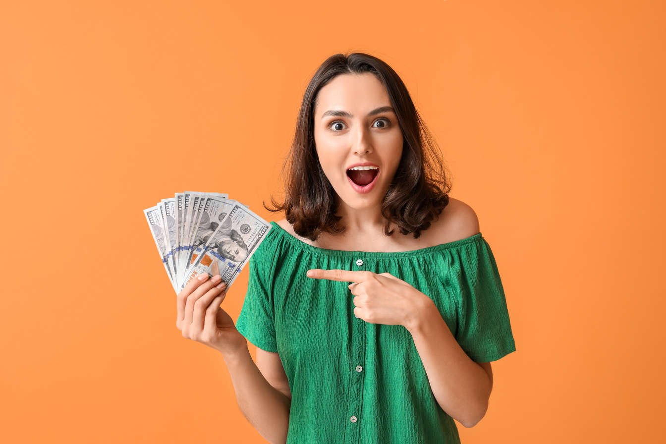 Surprised Young Woman with Money on Orange Background